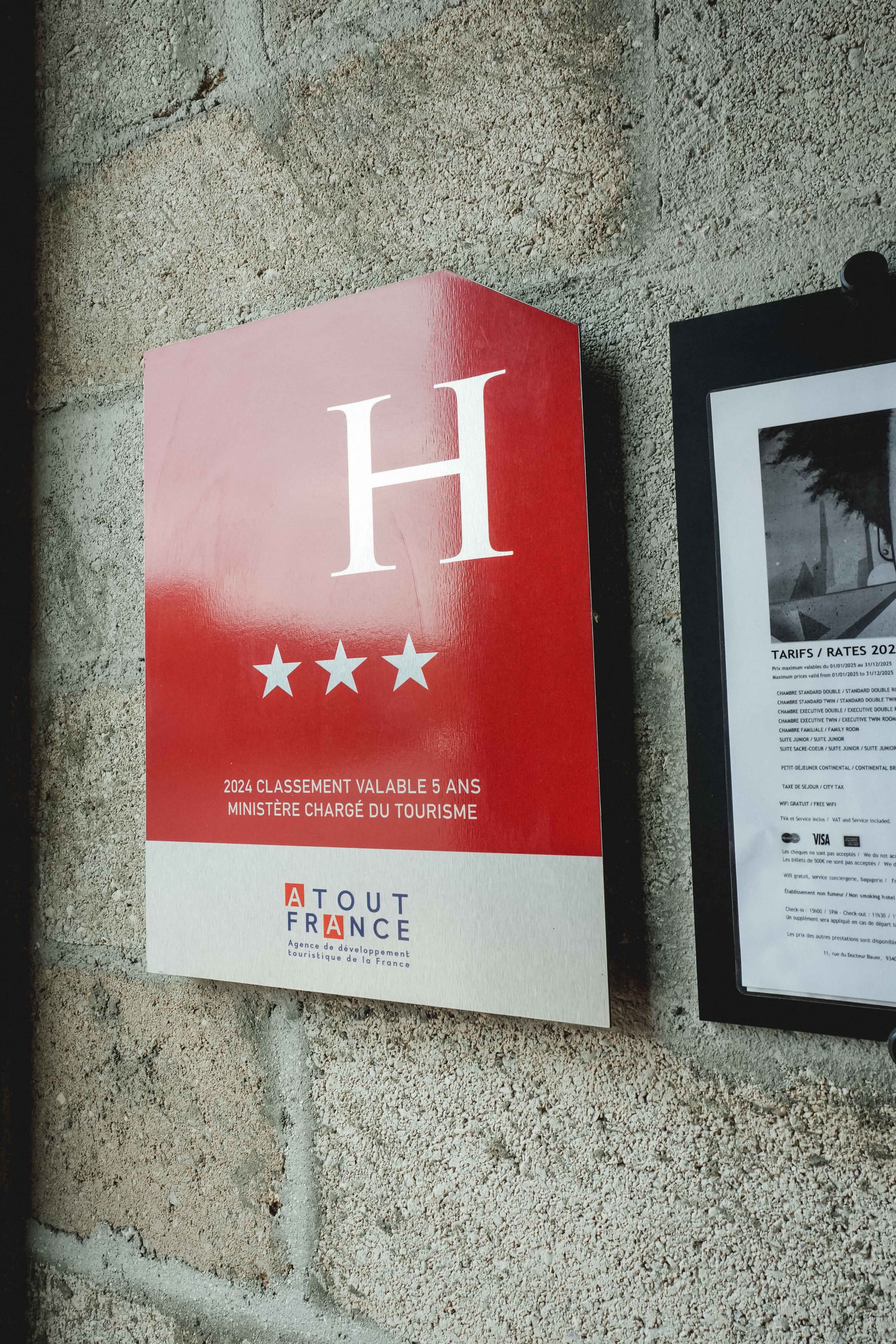 Plaque Atout France 3 étoiles sur mur béton brut · matière de la façade
